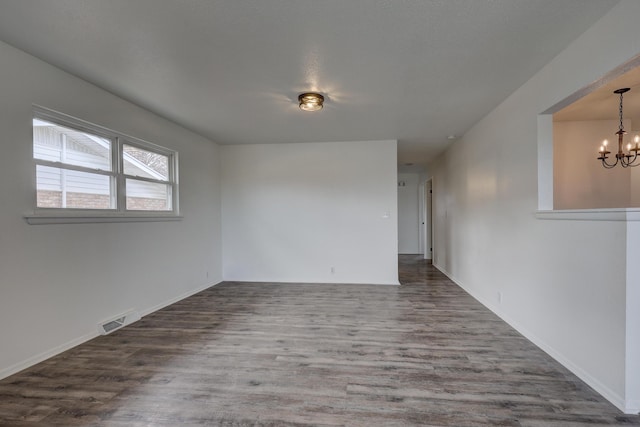 empty room with an inviting chandelier and dark wood-type flooring