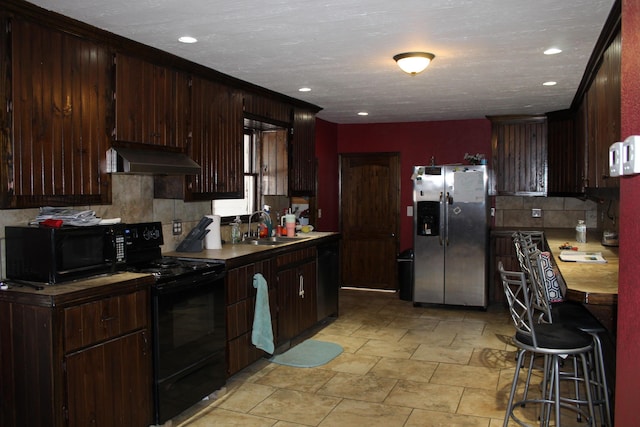 kitchen with sink, black appliances, dark brown cabinets, and wall chimney exhaust hood