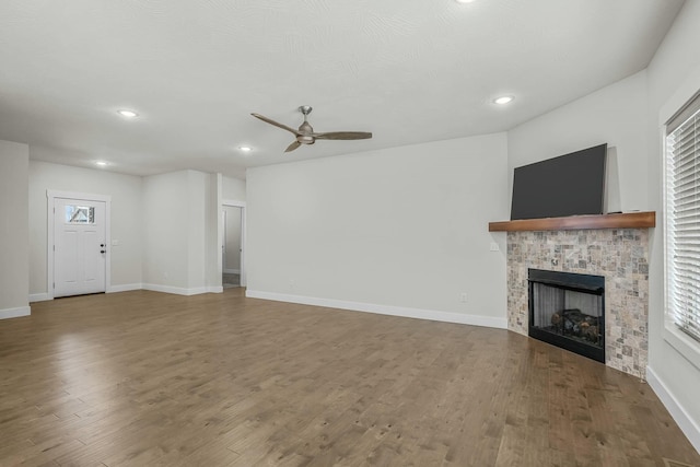 unfurnished living room with wood-type flooring, ceiling fan, and a stone fireplace