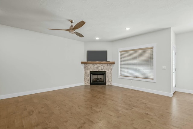 unfurnished living room with light wood-type flooring, ceiling fan, and a stone fireplace