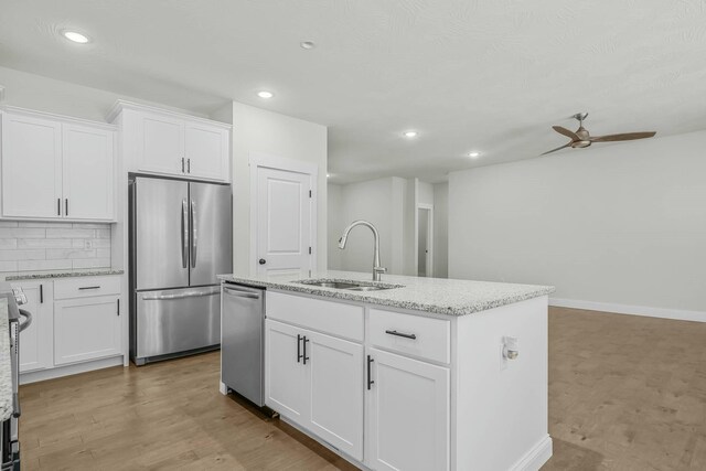 kitchen featuring stainless steel appliances, sink, white cabinets, tasteful backsplash, and an island with sink