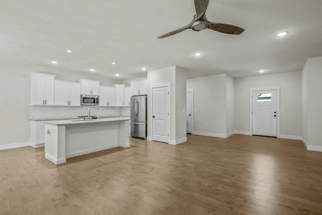 kitchen with a center island with sink, stainless steel appliances, ceiling fan, sink, and white cabinetry