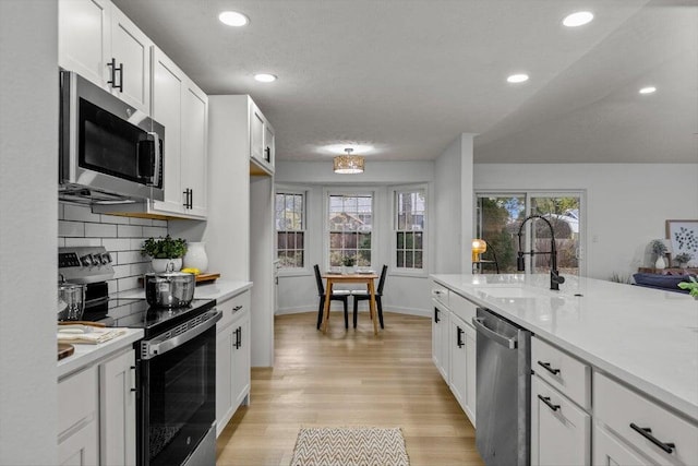 kitchen featuring light hardwood / wood-style floors, decorative backsplash, white cabinets, appliances with stainless steel finishes, and sink