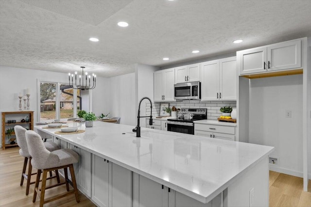 kitchen featuring a large island, an inviting chandelier, light wood-type flooring, white cabinetry, and appliances with stainless steel finishes