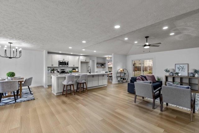 living room featuring lofted ceiling, a textured ceiling, light hardwood / wood-style floors, and ceiling fan with notable chandelier