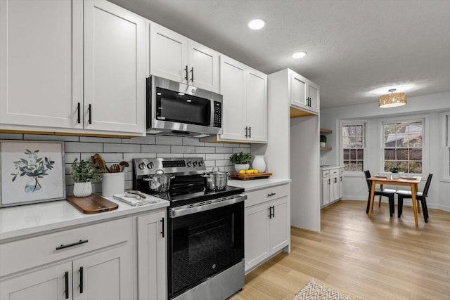 kitchen featuring stainless steel appliances, white cabinets, a textured ceiling, light wood-type flooring, and backsplash