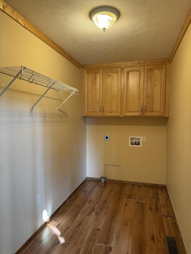 laundry room with a textured ceiling, light hardwood / wood-style flooring, electric dryer hookup, hookup for a washing machine, and cabinets