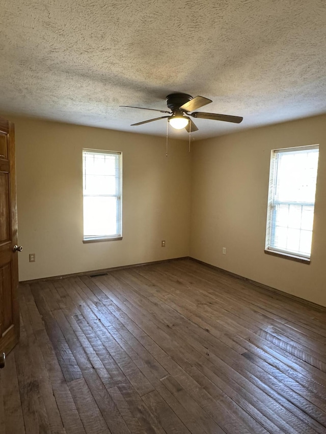 empty room featuring a textured ceiling, ceiling fan, plenty of natural light, and dark wood-type flooring