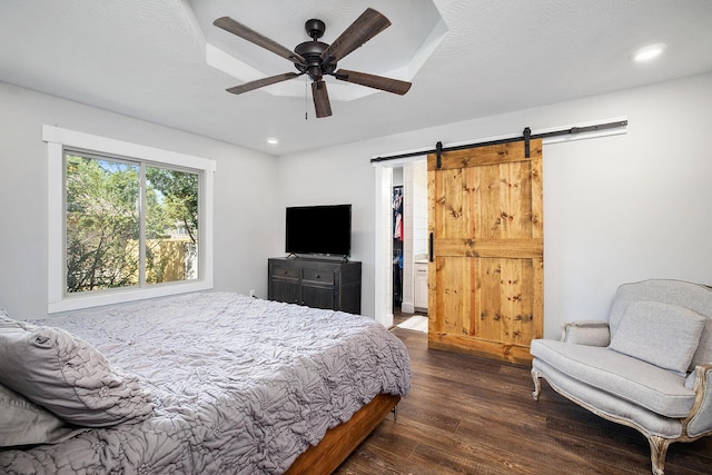 bedroom featuring ceiling fan, dark hardwood / wood-style floors, a textured ceiling, a spacious closet, and a barn door