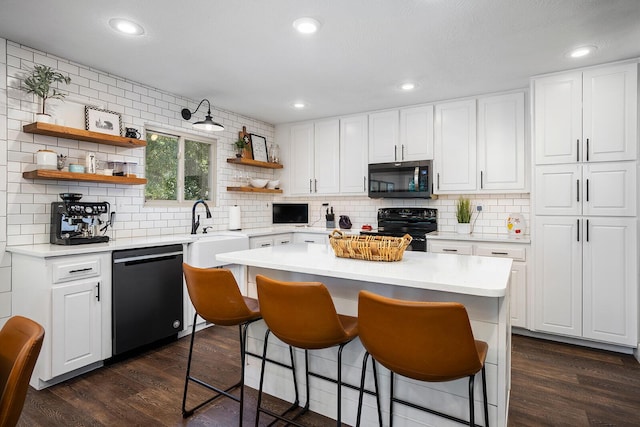 kitchen featuring white cabinets, a kitchen bar, a center island, black appliances, and dark wood-type flooring