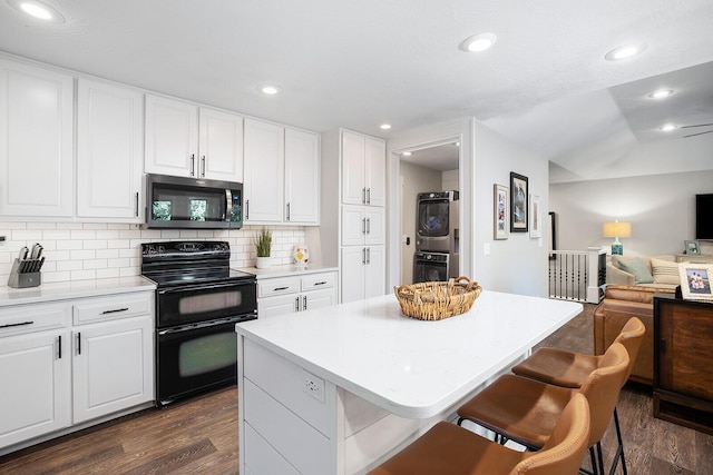 kitchen with a kitchen island, a breakfast bar, white cabinets, range with two ovens, and stacked washer / drying machine