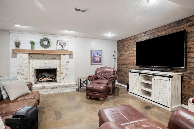 living room featuring wooden walls, a brick fireplace, concrete floors, and a textured ceiling