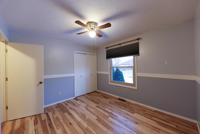 unfurnished bedroom featuring a closet, ceiling fan, a textured ceiling, and light hardwood / wood-style flooring