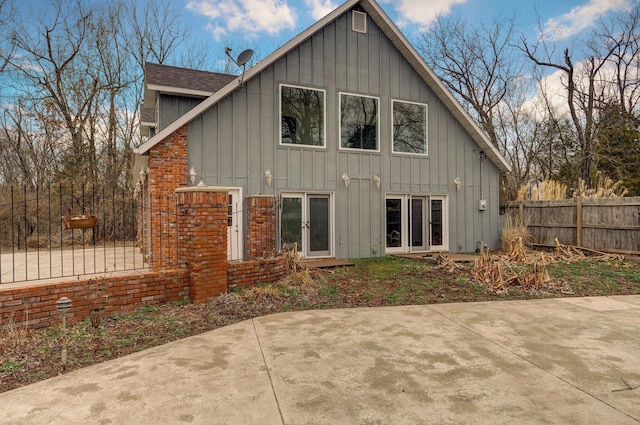 back of property featuring a patio, fence, roof with shingles, brick siding, and board and batten siding