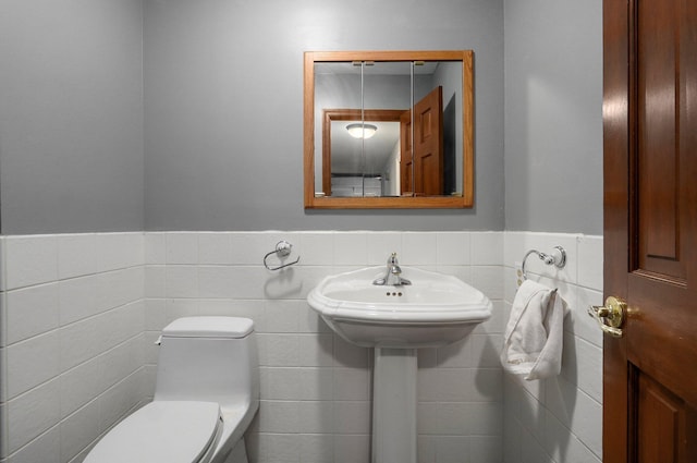 half bathroom with wainscoting, toilet, and tile walls