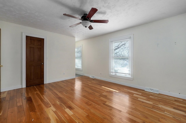 unfurnished room featuring a healthy amount of sunlight, a textured ceiling, baseboards, and hardwood / wood-style flooring