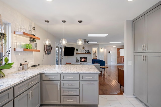 kitchen featuring a skylight, a fireplace, gray cabinets, light stone countertops, and a peninsula