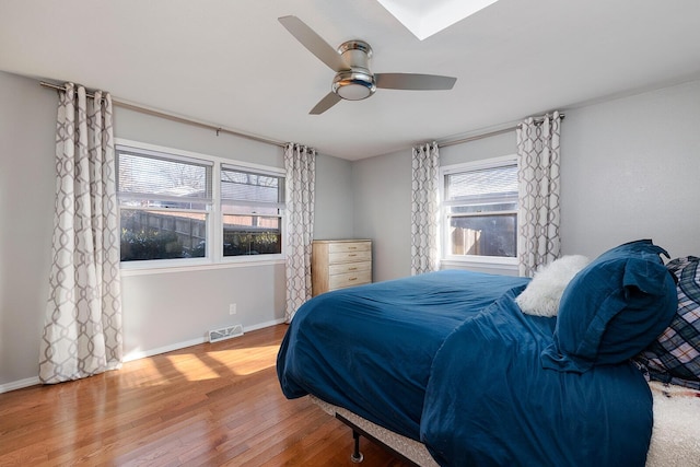 bedroom with ceiling fan, wood finished floors, visible vents, and baseboards