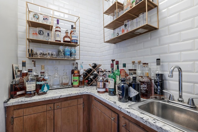 kitchen featuring a sink, backsplash, brown cabinets, light stone countertops, and open shelves