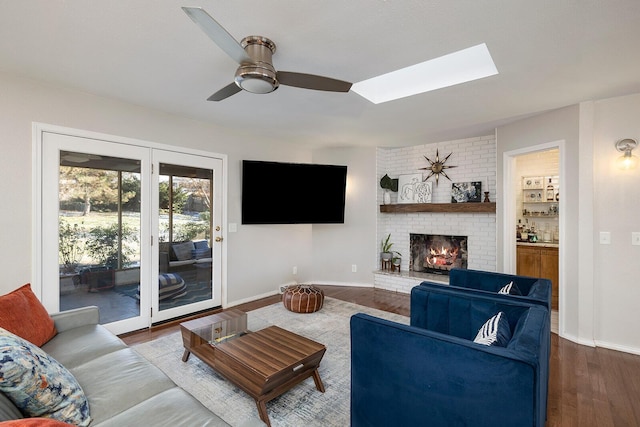 living room with dark wood-style flooring, a brick fireplace, a ceiling fan, and baseboards