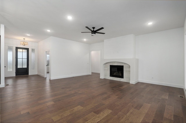 unfurnished living room featuring ceiling fan with notable chandelier, a fireplace, and dark hardwood / wood-style floors