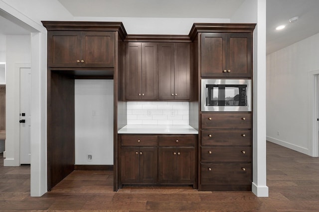 kitchen with stainless steel microwave, dark wood-type flooring, dark brown cabinetry, and decorative backsplash