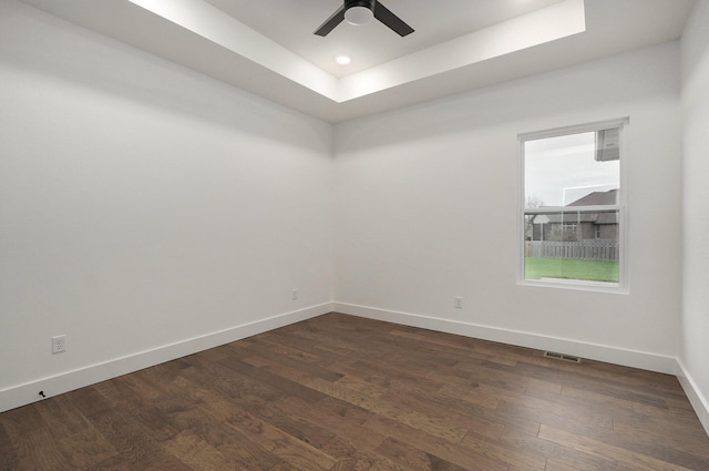 empty room with dark wood-type flooring, ceiling fan, and a tray ceiling