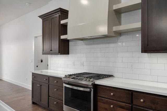 kitchen featuring stainless steel gas stove, dark brown cabinetry, decorative backsplash, dark hardwood / wood-style floors, and range hood