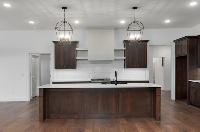 kitchen with hanging light fixtures, a kitchen island with sink, and dark brown cabinets