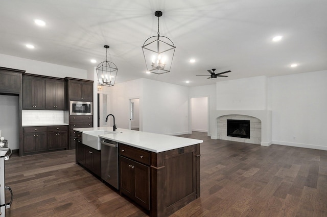 kitchen with hanging light fixtures, an island with sink, a fireplace, appliances with stainless steel finishes, and sink