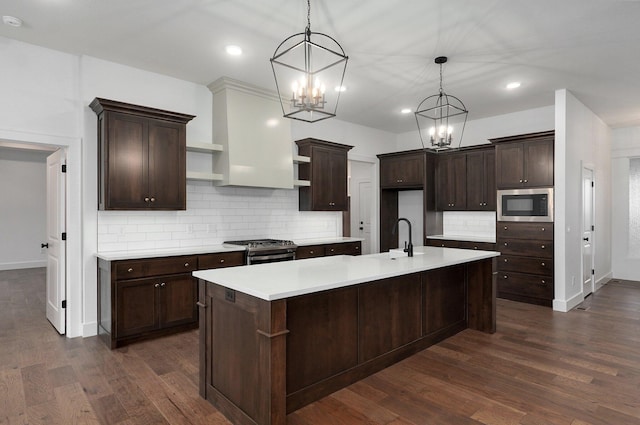 kitchen with hanging light fixtures, an island with sink, stainless steel gas stove, and built in microwave