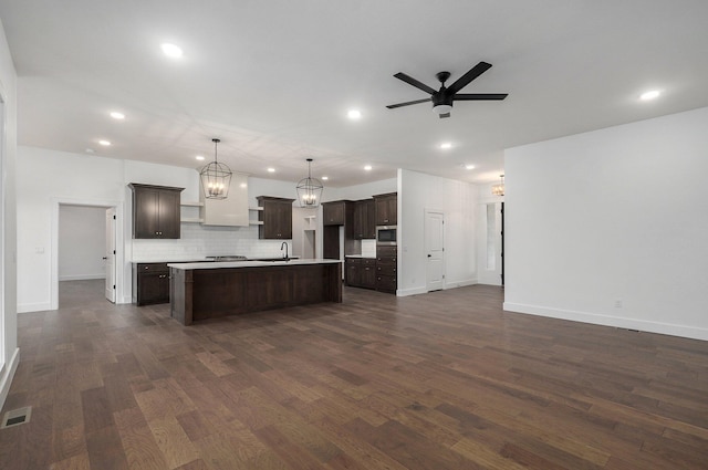 kitchen featuring decorative light fixtures, ceiling fan, dark brown cabinetry, dark hardwood / wood-style floors, and a kitchen island with sink