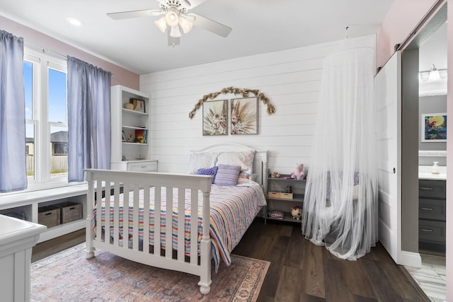 bedroom with hardwood / wood-style floors, ensuite bath, a barn door, ceiling fan, and wooden walls