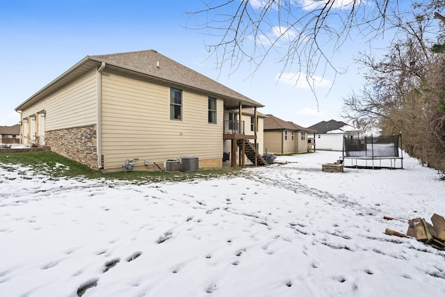 snow covered back of property with central AC and a trampoline