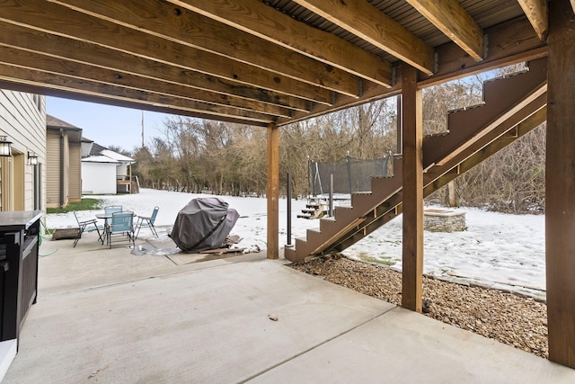 snow covered patio with area for grilling and a trampoline