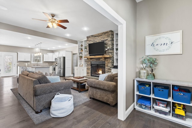 living room featuring sink, ceiling fan, built in features, dark hardwood / wood-style floors, and a stone fireplace