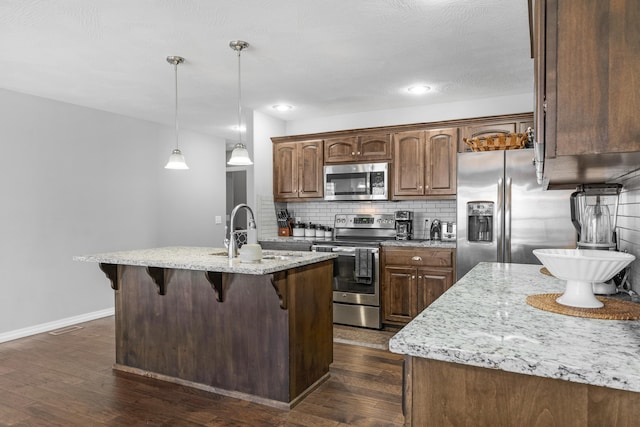 kitchen featuring stainless steel appliances, sink, decorative backsplash, hanging light fixtures, and a kitchen island with sink