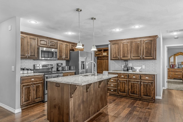 kitchen with pendant lighting, tasteful backsplash, a kitchen island with sink, appliances with stainless steel finishes, and sink