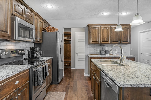 kitchen with sink, appliances with stainless steel finishes, backsplash, a kitchen island with sink, and dark wood-type flooring