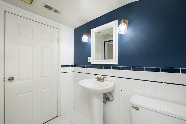 bathroom with toilet, tile patterned floors, tile walls, and sink