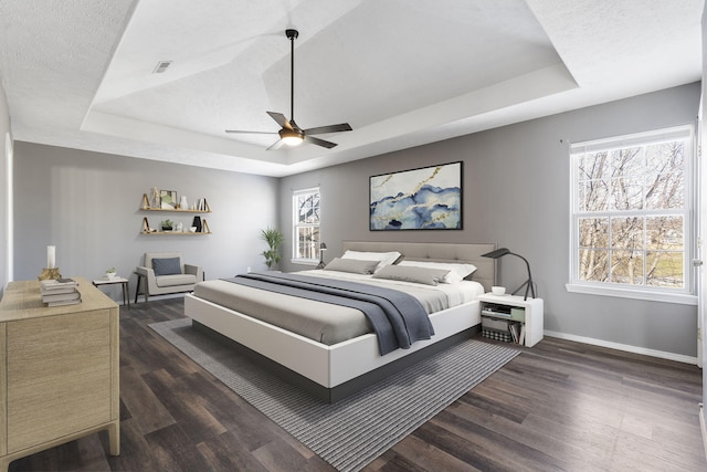 bedroom featuring ceiling fan, dark hardwood / wood-style floors, and a tray ceiling