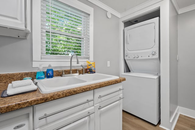 laundry area featuring sink, stacked washer and clothes dryer, ornamental molding, and light hardwood / wood-style floors