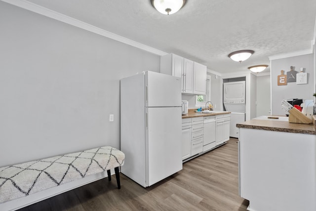 kitchen with a textured ceiling, white cabinets, stacked washer / drying machine, white fridge, and sink