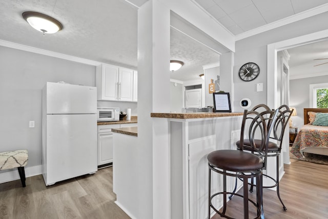 kitchen featuring a breakfast bar, kitchen peninsula, white appliances, white cabinetry, and ornamental molding