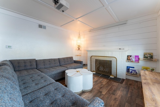 living room featuring dark wood-type flooring, wood walls, coffered ceiling, and a brick fireplace