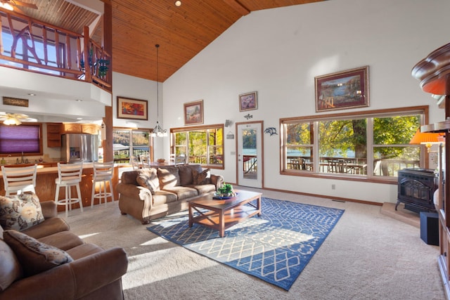 carpeted living room with wood ceiling, high vaulted ceiling, a wood stove, and ceiling fan with notable chandelier