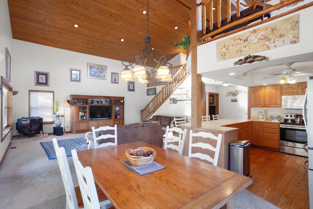 dining area with ceiling fan with notable chandelier, high vaulted ceiling, wood ceiling, and a wood stove