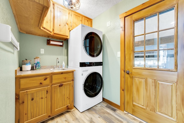 washroom with cabinets, stacked washer and clothes dryer, a textured ceiling, sink, and light hardwood / wood-style flooring