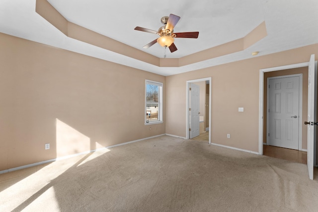 unfurnished bedroom with ensuite bathroom, a raised ceiling, light carpet, and ceiling fan