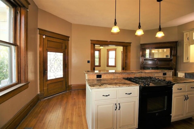 kitchen featuring black gas range, hardwood / wood-style flooring, white cabinets, stone countertops, and decorative light fixtures